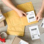 haende kleben versandetikett auf paket und briefumschlag mit laptop im hintergrund